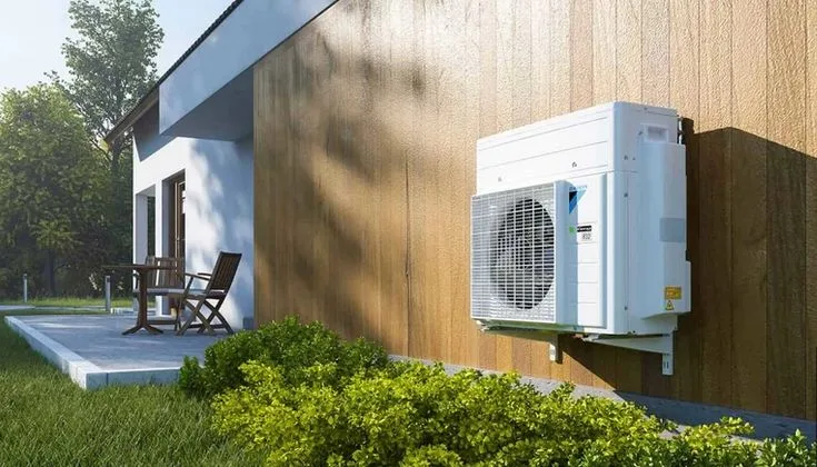 Unidad exterior de aerotermia instalada en la fachada de una vivienda con terraza